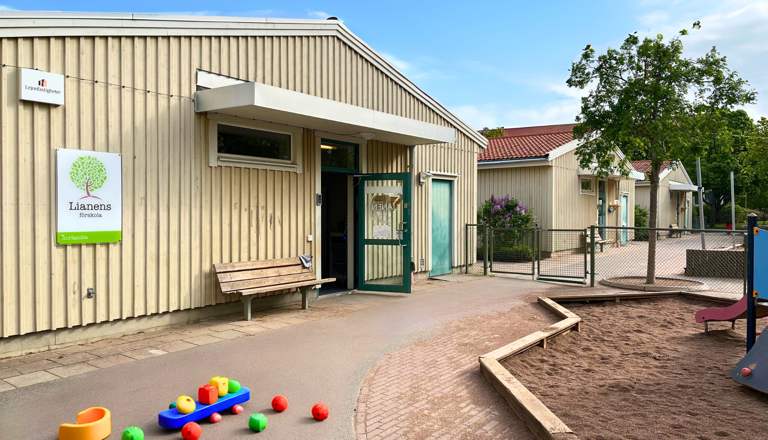 Ljus förskolebyggnad med sandlåda, lekredskap och grönska – en trygg miljö för nyfikenhet, lek och gemenskap.