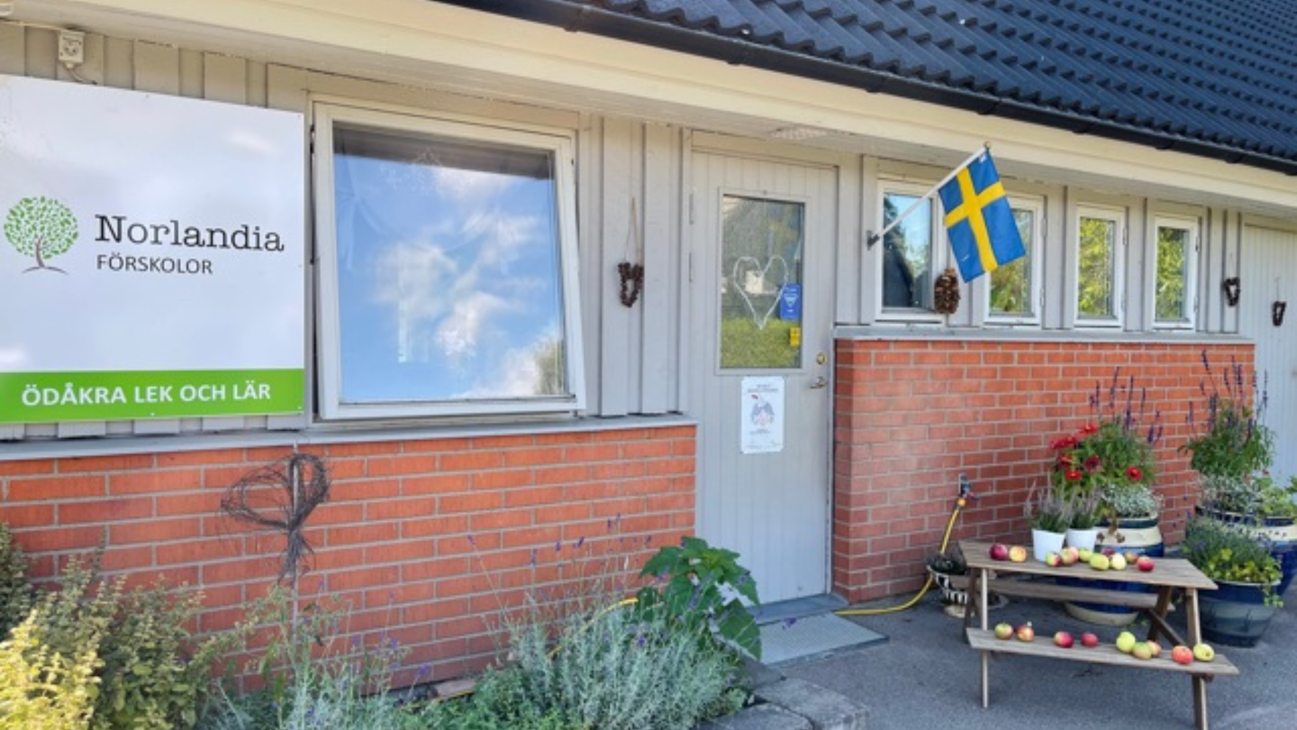 Entré med skylt, svenska flaggan och bord fullt av äpplen – en välkomnande plats för lek, lärande och gemenskap.