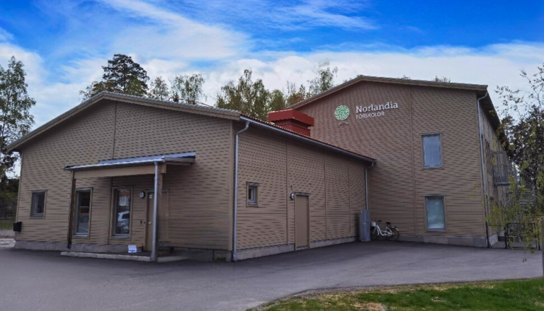 Modern förskolebyggnad i trä med Norlandia-logotyp, omgiven av träd – en trygg plats för lek, gemenskap och nya upptäckter.