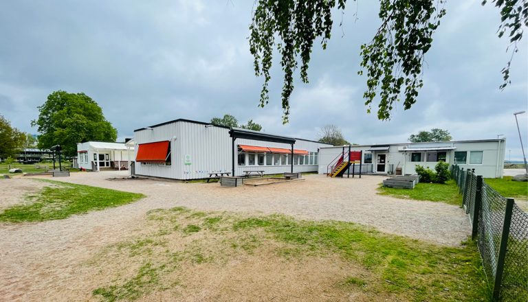 Ljus förskolebyggnad med utegård, lekytor och markiser – en öppen plats för trygghet, gemenskap och rörelseglädje.