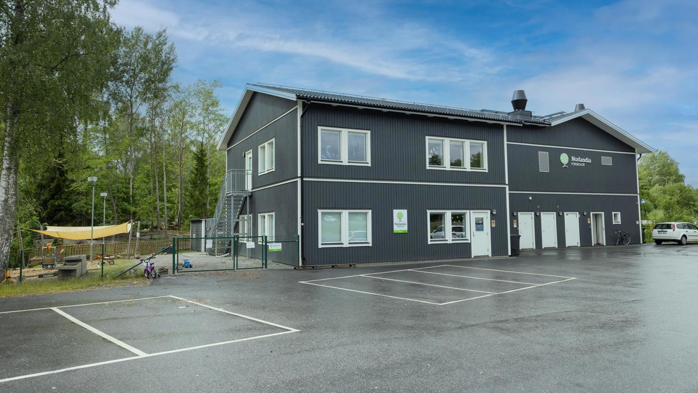 Mörkblå förskolebyggnad med lekplats i vintrig miljö – en trygg plats för lek, gemenskap och upptäckter bland snö och natur.