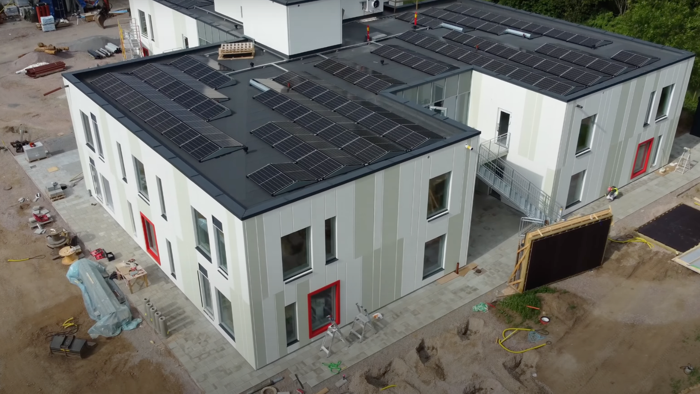 Nybyggd förskolebyggnad i två plan med solpaneler på taket och färgstarka detaljer runt fönstren.