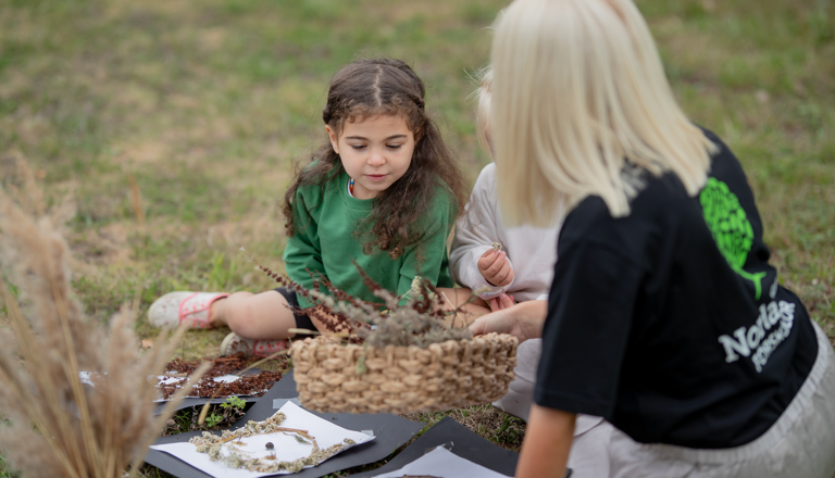 Pedagog från Norlandia Förskolor sitter ute med barn och utforskar naturmaterial.