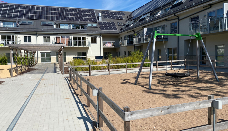 Förskola i modern innergårdsmiljö med sandlåda och kompisgunga – en trygg plats för rörelse, lek, glädje och gemenskap.