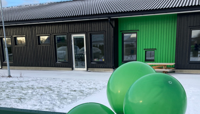 Ny förskolebyggnad i svart och grönt med snötäckt gård och gröna ballonger – en färgglad start i vintermiljö.