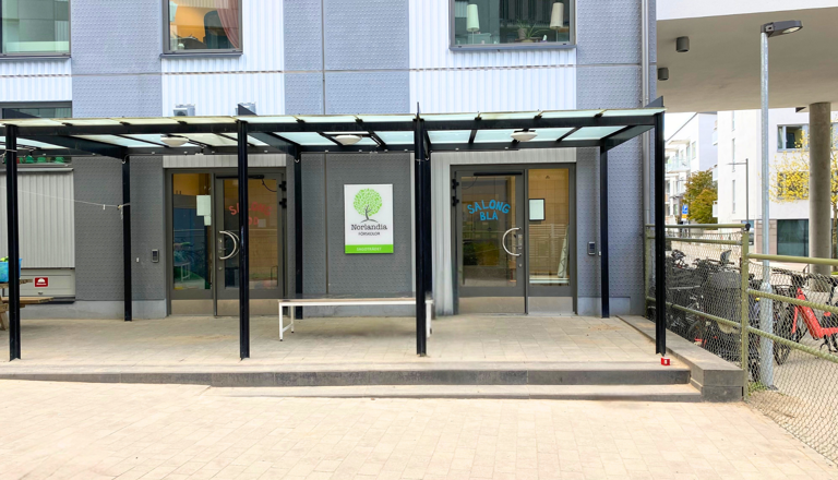 Entré till Norlandia Förskolor Sagoträdet med glasdörrar och takskydd – en trygg plats mitt i stadens puls.