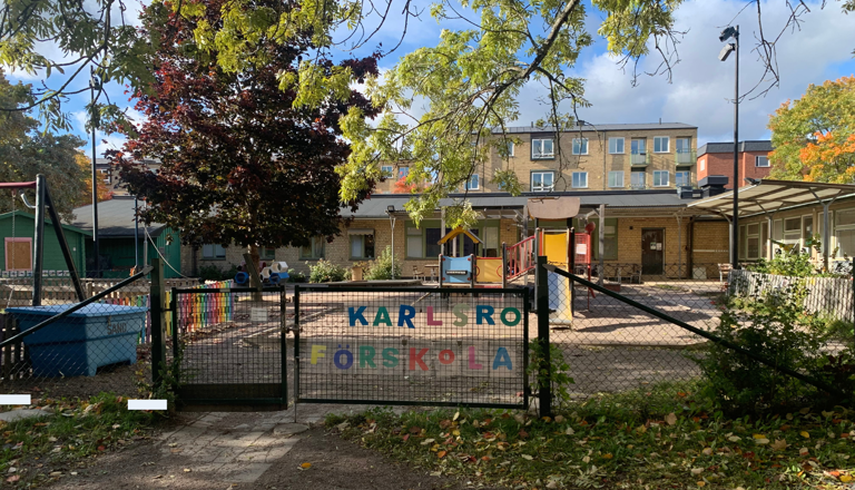 Förskolegård med grind, lekställning och färgglad skylt i trädkant – en trygg plats för lek, glädje och gemenskap.