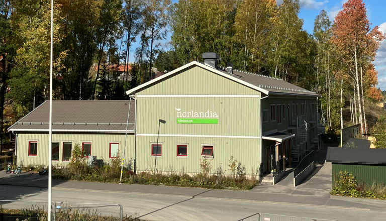 Grön förskolebyggnad med skog i bakgrunden – en trygg plats där barn får utforska, leka och lära nära naturen.