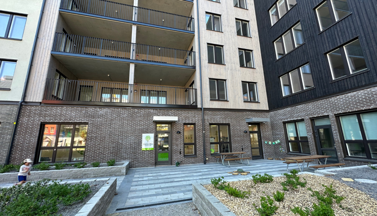 Modern förskoleentré i tegelhus med utegård, planteringar och lek – trygg plats för lärande mitt i stadsmiljö.