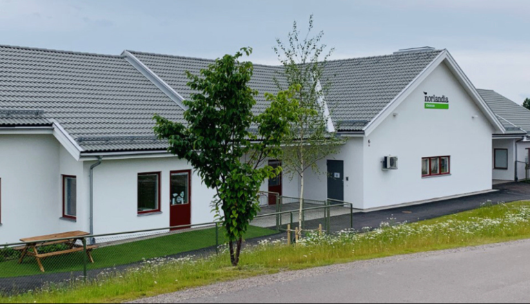 Vit enplansförskola med grått sadeltak och grön utemiljö – en trygg, lugn plats för lek, nyfikenhet, gemenskap och upptäckter