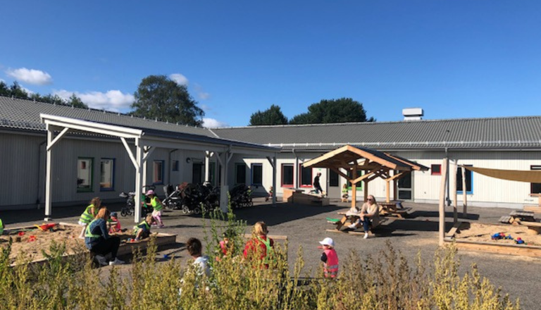 Förskola med stor gård där barn leker i sandlådor och vid sittgrupper – en trygg plats för lek, rörelse och gemenskap.