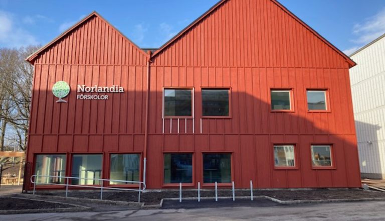 Röd tvåvåningsbyggnad med Norlandia Förskolor-logotyp på fasaden, stora fönster och ramp vid entrén.