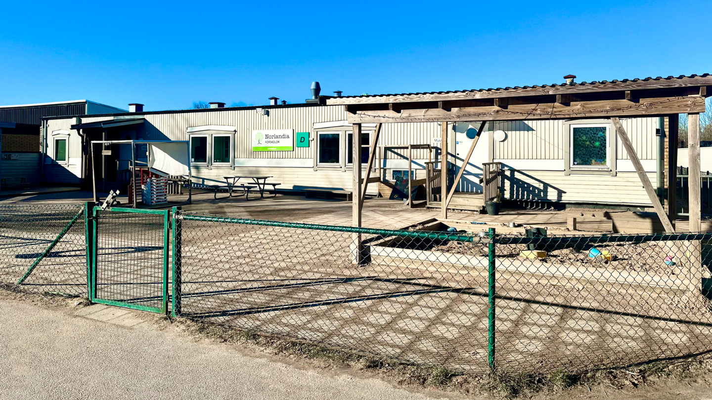 Förskolegård med trähus, lekplats och sandlåda i soligt väder – en plats där barn får leka, utforska och växa varje dag.