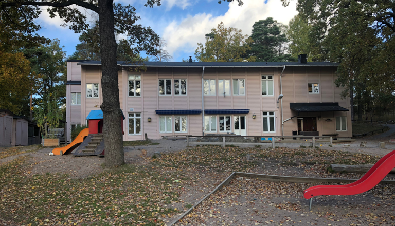 Ljus tvåvånings förskola i trä med lekplats framför – en trygg plats för lek, gemenskap, utforskande och lärande.