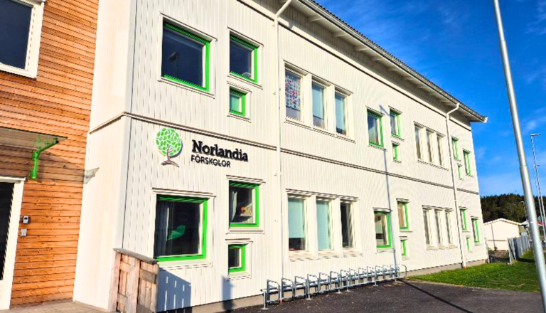 Ljus fasad med gröna fönsterdetaljer och Norlandia Förskolor-logga, soligt väder och blå himmel.