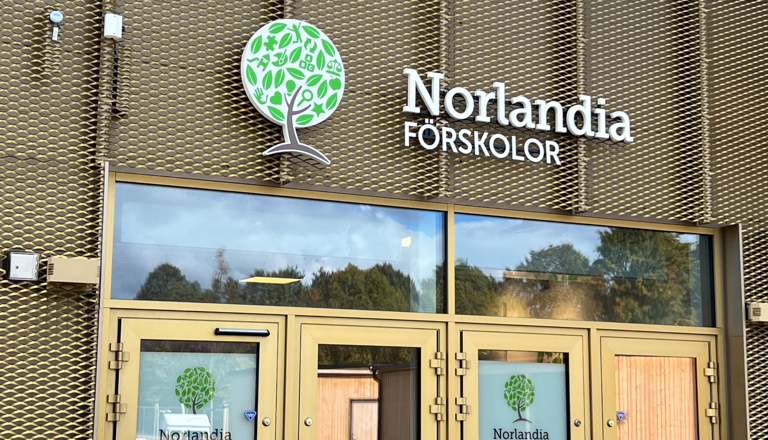Entré med Norlandia Förskolors logotyp på guldfärgad fasad – en välkomnande plats för nya upptäckter varje dag.