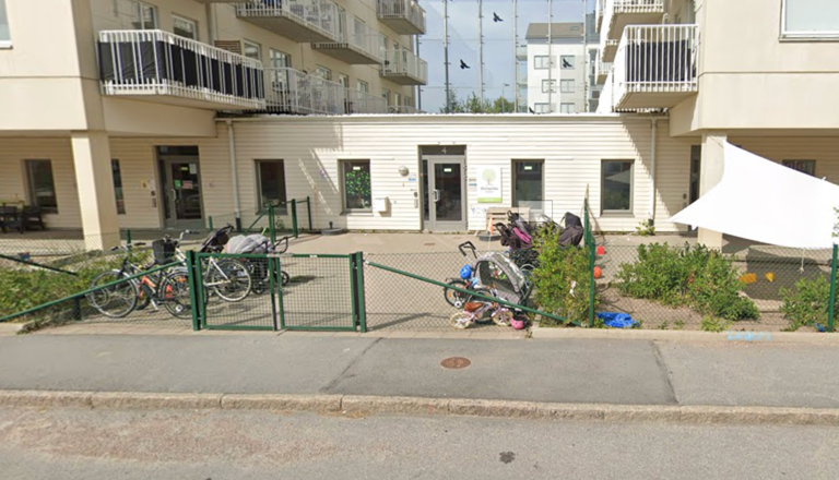 Förskoleentré i markplan med barnvagnar, cyklar och grönska – en trygg startpunkt för lek, omsorg och gemenskap.