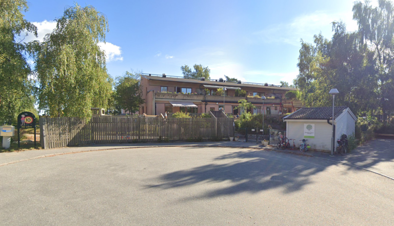 Förskola i ett grönskande bostadsområde med träd, staket och cyklar – en trygg plats för lek, gemenskap och upptäckarglädje.